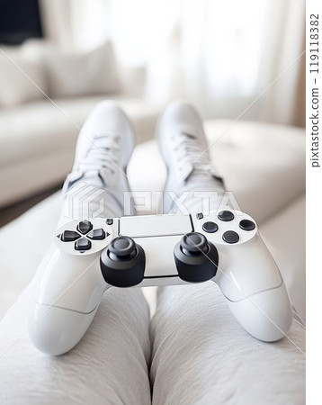Person in white sneakers reclining on sofa with white game controller, showcasing a casual and comfortable gaming setup in a modern living room Person in white sneakers reclining on sofa with white game controller, showcasing a casual and comfortable gaming setup in a modern living room 119118382
