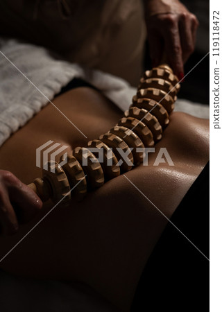 Anti-cellulite massage on the stomach using wooden objects. Massage salon in a dark room. 119118472