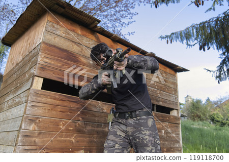 a young sniper aims at a house from the woods 119118700