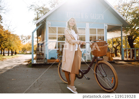 Beautiful woman with a bike on the background of a blue house in the fall. 119119328