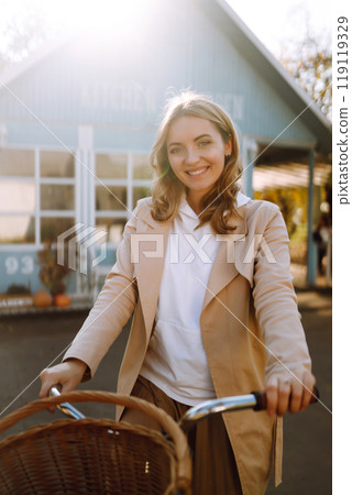 Beautiful woman with a bike on the background of a blue house in the fall. 119119329