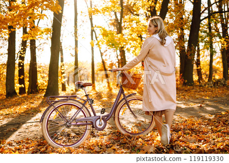 Stylish woman with a bicycle enjoying autumn weather in the park. Beautiful Woman in the autumn forest. 119119330