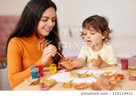 Cute little girl and mom spending good time painting hands and autumn yellow leaves together 119119432