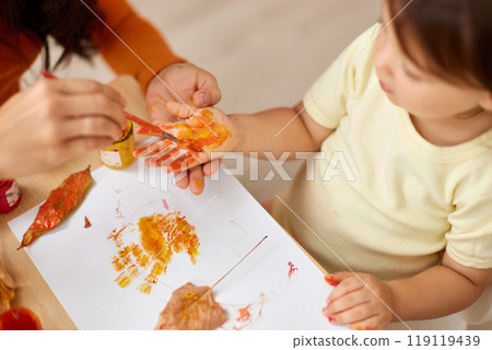 close-up, child and mom hands painting autumn yellow leaves together. happy time together at home 119119439