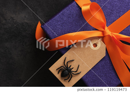 Halloween gift wrapped in purple paper with orange ribbon and empty label with spider on it 119119473