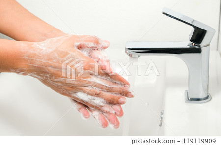 Hands of woman wash their hands in a sink with foam to wash the skin and water flows through the hands. Concept of health, cleaning and preventing germs and coronavirus from contacting hands 119119909