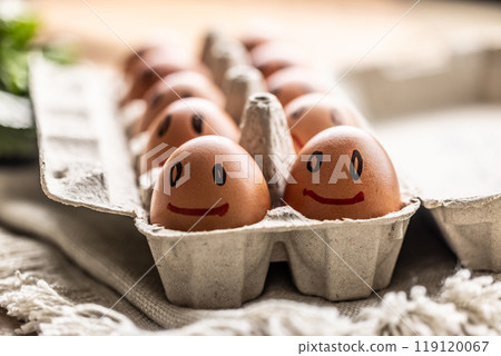 Cute smiling fresh eggs in a paper carton on the kitchen table 119120067