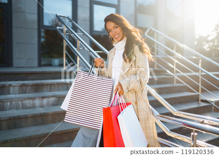 Stylish woman with shopping bags walks through city streets. Purchases, shopping, lifestyle concept. Stylish woman with shopping bags walks through city streets. Purchases, shopping, lifestyle concept. 119120336