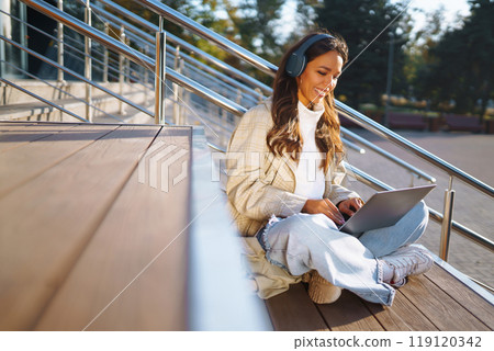 Young woman in headphones with laptop on city street. Video conference. ?nline training. Freelancer 119120342