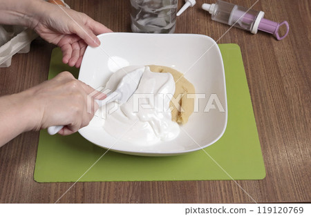 Dough preparation process. Woman mix in bowl powdered sugar, almond flour and beaten egg white using silicone spatula. Baking macarons at home. Close-up of hands. 119120769
