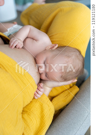 Mother breastfeeding her newborn baby while sitting comfortably at home Mother breastfeeding her newborn baby while sitting comfortably at home 119121180