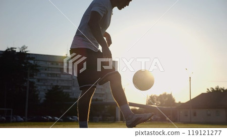 Professional footballer juggling soccer ball on stadium at sunset. Young man kicking ball at green field. Sportsman practicing tricks at meadow with sunlight at background. Freestyle football concept Professional footballer juggling soccer ball on stadium at sunset. Young man kicking ball at green field. Sportsman practicing tricks at meadow with sunlight at background. Freestyle football concept 119121277