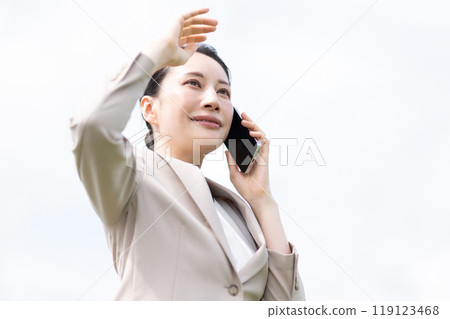 A woman in a suit holding a smartphone who is concerned about the sunlight A woman in a suit holding a smartphone who is concerned about the sunlight 119123468