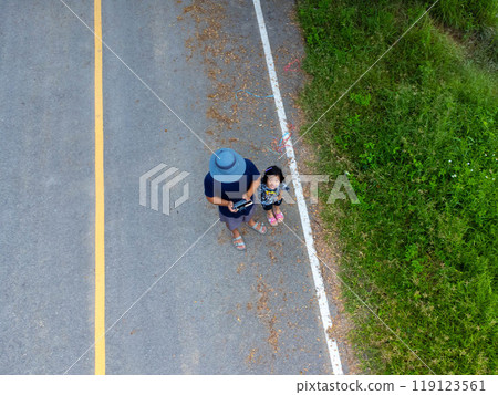 Drone view of father and daughter standing on asphalt road against natural green rural background. Drone view of father and daughter standing on asphalt road against natural green rural background. 119123561