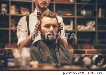 Looking amazing. Close-up of hairdresser checking symmetry of haircut of his client at barbershop 119124393