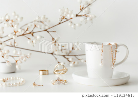 Gold jewelry and a branch of white flowers on a white surface 119124613