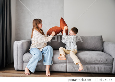 Two young siblings started a pillow fight on couch. Little boy and her older sister fighting by pillows. Funny spending time with family at home. Two young siblings started a pillow fight on couch. Little boy and her older sister fighting by pillows. Funny spending time with family at home. 119125077