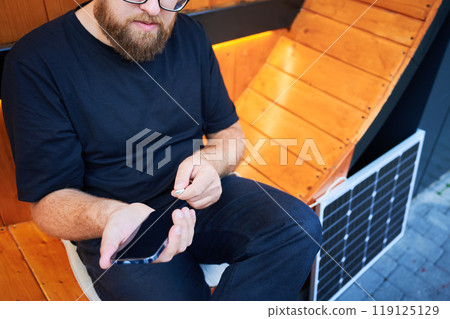 Cropped view of man connecting smartphone to photovoltaic solar panel. Integration of sustainable renewable energy into everyday life, demonstrating practical use of solar power for charging devices. Cropped view of man connecting smartphone to photovoltaic solar panel. Integration of sustainable renewable energy into everyday life, demonstrating practical use of solar power for charging devices. 119125129