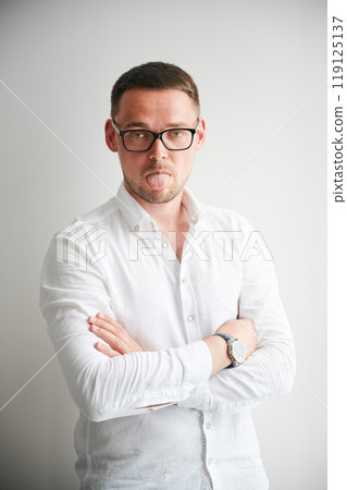 Portrait of man sticking his tongue out in a playful manner. Handsome young male in casual clothes keeping arms crossed while standing on white background. Portrait of man sticking his tongue out in a playful manner. Handsome young male in casual clothes keeping arms crossed while standing on white background. 119125137