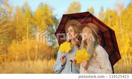 Happy two women friends with autumn yellow leaves, holding umbrella, smiling girlfriends in park Happy two women friends with autumn yellow leaves, holding umbrella, smiling girlfriends in park 119125423