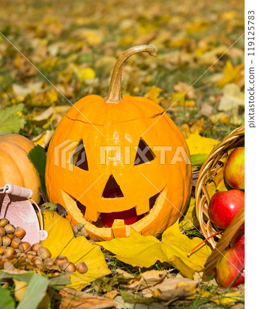 Pumpkin - head and basket with apples on a background of yellow leaves. 119125783