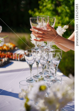 Female hands building a champagne tower out of glasses. 119125865