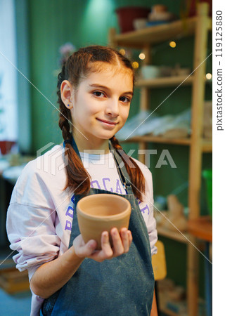 A teenage girl with long dark hair sculpts from clay in a pottery workshop. A teenage girl with long dark hair sculpts from clay in a pottery workshop. 119125880