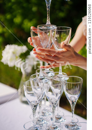 Female hands building a champagne tower out of glasses. Female hands building a champagne tower out of glasses. 119126068