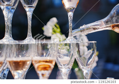 Champagne or sparkling wine is poured into glasses.  119126103
