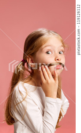 Girl playing with hair looking serious with wide eyes, and makes mustache, adding sense of curiosity or mischief to her facial expression. 119126112