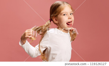 Vibrant portrait of little girl sticks out her tongue while playing with pigtails, moment of pure fun and mischief as she enjoys lighthearted moment. 119126127