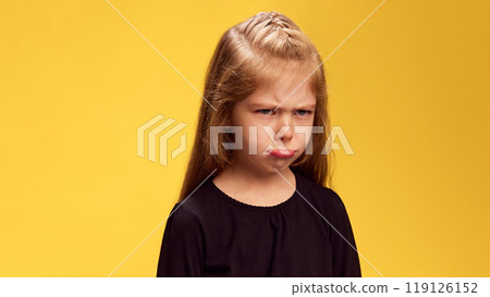 Girl's pouty face, complete with furrowed brows, perfectly conveys mood of frustration or sadness against yellow studio background. 119126152