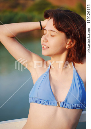 Cute slim young woman in blue swimsuit on a bridge by river 119126153