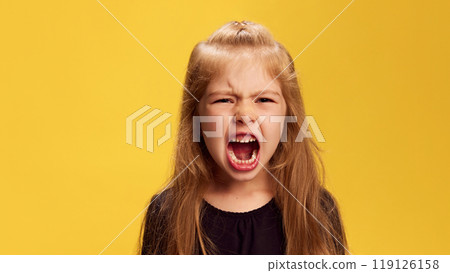 Little girl lets out loud, powerful yell, showing her temper against yellow studio background. Raw expression of anger or frustration. Little girl lets out loud, powerful yell, showing her temper against yellow studio background. Raw expression of anger or frustration. 119126158