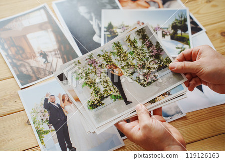 Men's hands put on the wooden table and show wedding photos. 119126163