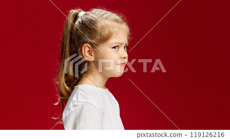 Little girl looks deeply thoughtful, her hand resting under her chin in classic thinking pose, as though pondering something important against red background. Little girl looks deeply thoughtful, her hand resting under her chin in classic thinking pose, as though pondering something important against red background. 119126216