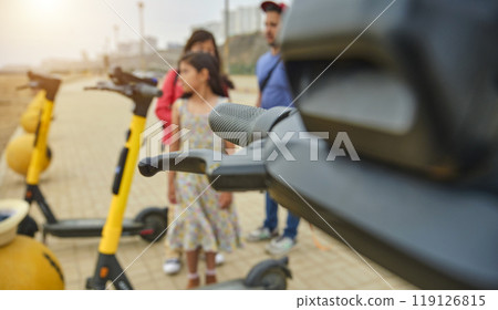 A group of people are standing around a row of scooters. Summer time. Selective focus. 119126815