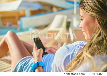 Young Beautiful using mobile phone sitting on chair in swimming pool. 119126829