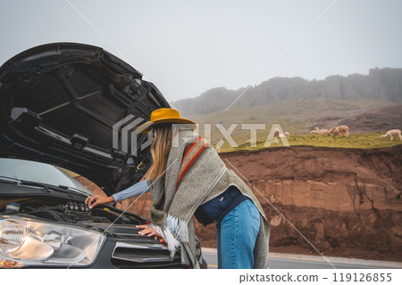 A woman in a yellow hat is standing next to a car with the hood up, tourist in Huayllay, Peru. 119126855