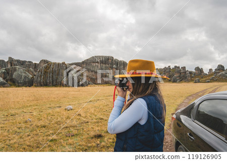 A woman wearing a yellow hat is taking a picture of a rocky landscape. Huayllay Stone Forest, Peru. 119126905