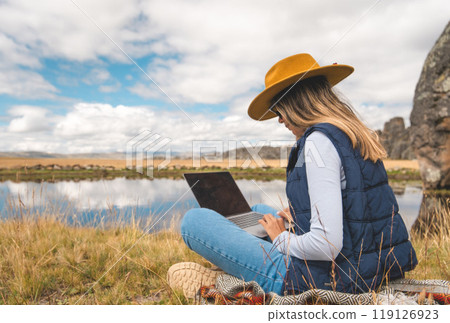 A woman is sitting on the grass with a laptop in front of her. Huayllay Stone Forest, Peru. 119126923