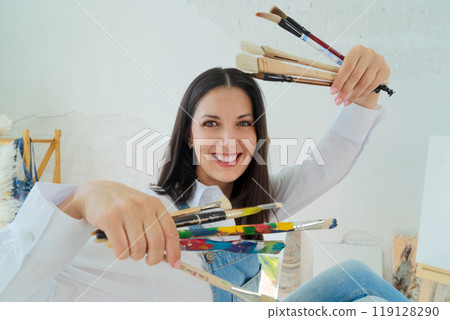 A Joyful Artist Proudly Showcasing Their Colorful Paint Brushes in a Bright and Inspiring Studio Environment 119128290