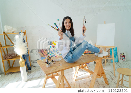A Joyful Artist Proudly Showcasing Their Colorful Paint Brushes in a Bright and Inspiring Studio Environment 119128291