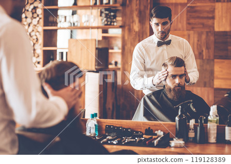 Looking amazing. Hairdresser checking symmetry of haircut of his client in front of mirror at barbershop Looking amazing. Hairdresser checking symmetry of haircut of his client in front of mirror at barbershop 119128389
