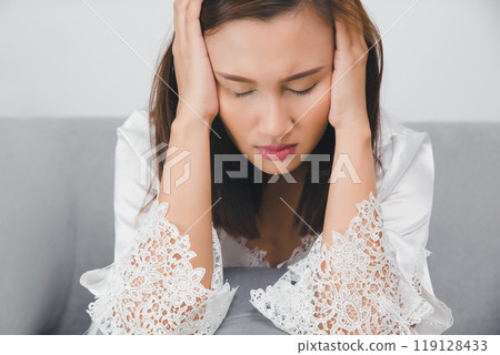 A woman in a white nightgown appears to be experiencing headache at night. A woman in a white nightgown appears to be experiencing headache at night. 119128433