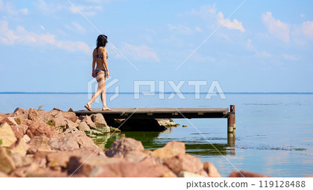 Young pretty woman in swimsuit going on pier on shore Young pretty woman in swimsuit going on pier on shore 119128488