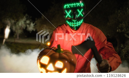 Anonymous Man in Glowing Mask with Halloween Pumpkin And Axe Anonymous Man in Glowing Mask with Halloween Pumpkin And Axe 119128626