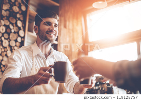 Here is your coffee! Close-up part of young handsome man in apron giving two coffee cups to his customer while standing at cafe Here is your coffee! Close-up part of young handsome man in apron giving two coffee cups to his customer while standing at cafe 119128757