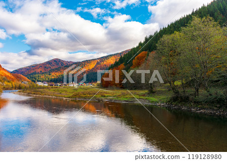 autumn landscape with tereblya river in carpatian mountains. countryside scenery of ukraine on a cloudy day in fall season reflecting in the calm water. village in the distance. scenic view 119128980