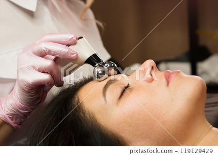 Cosmetologist performing phonophoresis ultrasound therapy on woman's face 119129429